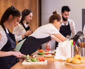 Cooking course - senior male chef in cook uniform teaches young people cooking class students to prepare and mix ingredients for dishes in restaurant kitchen