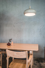 Wooden table and chair with lighting lamp and flower vase on cement wall
