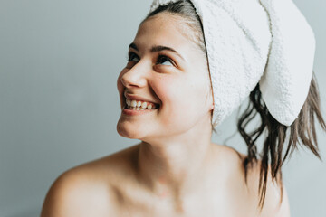 Pretty calm smiley woman with wrap towel on head, enjoys softness of glowing skin and hair...