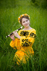 little smiling child in yellow dress sitting in the green meadow and playing music by flute © Tetatet