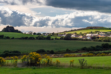 Obraz premium Sky with cumulus clouds over a Irish village on evening. Irish settlement in County Cork, landscape. European countryside, rustic landscape. Green grass field under cloudy sky
