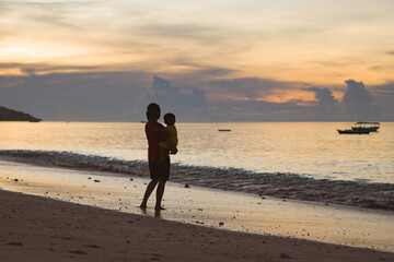 Naklejka premium mother holding her child for a walk on the beach at sunset