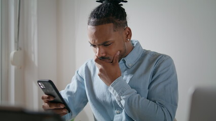 Annoyed guy using mobile phone at flat. Irritated man looking smartphone screen