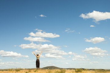 red-haired woman with outstretched arms in a meadow with white clouds and blue sky in the background