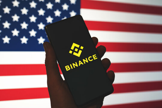 Binance app logo on smartphone in hand with blurred American flag background. Binance in the USA news. Crypto exchange, trading platform. Swansea, UK - July 27, 2021.