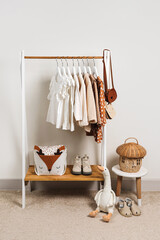 Clothing Rack with kids outfits and storage baskets in children's room. Fashion clothes in white, beige and brown colors on hangers in wardrobe. Set of kids clothes and accessories.