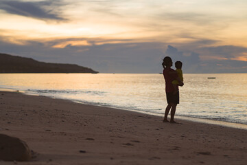 Naklejka premium mother holding child on the beach at sunset