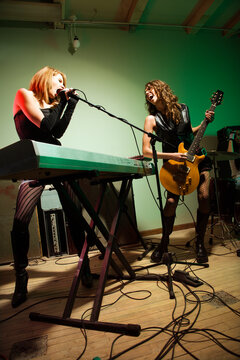 Two caucasian girls singing into microphone and playing the guitar.