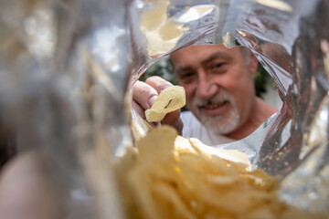 Persona mayor de día, sacando papas fritas con perspectiva desde la bolsa, cara desenfocada, manos...