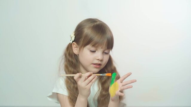 A little preschool girl with brown hair paints palms of different colors. Sensory development and experiences, themed activities with children, fine motor skills development.