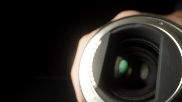 The camera lens is in my hands, I look at it on a black background and bring it close.