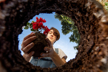 Mujer joven plantando una planta con flor de día. Perspectiva especial desde adentro de la tierra