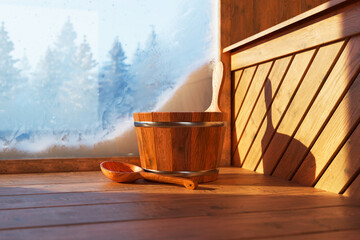 Wooden sauna bucket on the floor with winter day forest behind a frosty window