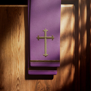 Purple stole with cross lightened by rays of light falling into a confessional.
