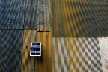 Solar panel attached on old zinc wall. Electric solar panel on the house wall. Small solar panel mounted on an outdoor galvanized wall with copy space. Using renewable solar energy technology concept. - obrazy, fototapety, plakaty