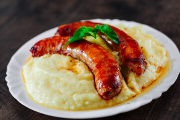 fried meat sausages with mashed potatoes in white plate on wooden table background