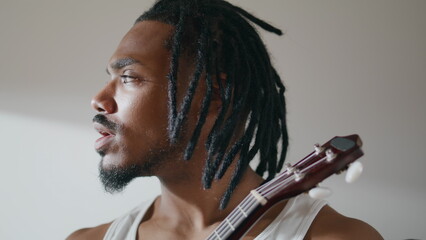 Thoughtful guy enjoying ukulele at apartment closeup. Involved man playing song