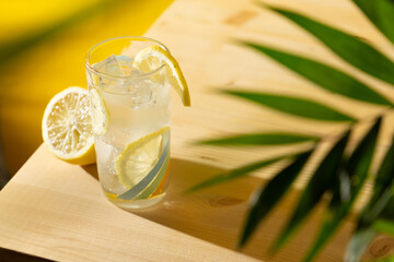 Top angle view of a lemonade glass with ice cubes on a wooden table and palm leaf
