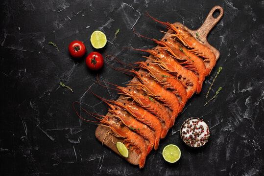 Large langoustines on a wooden board, black stone background. Top view, flat lay. Red boiled langoustine.