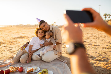Creating memories. Father clicking picture of family at beach, woman and sons posing for photo during picnic by seaside