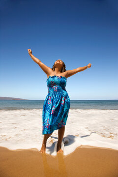 Yound-adult Black woman standing in shore with arms stretched.