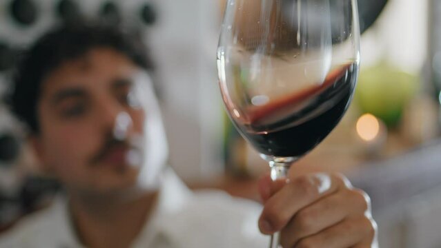 Man swirling red wine in glass goblet checking quality grape alcohol close up.