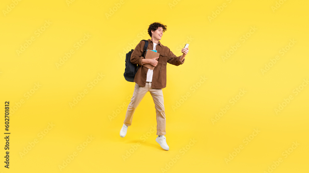 Poster joyful student guy using smartphone learning on-the-go over yellow background