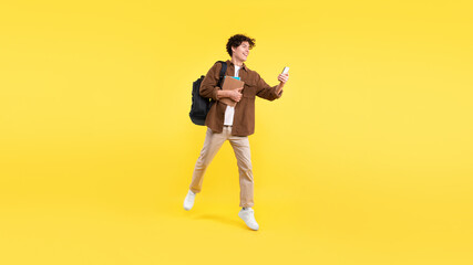 Fototapeta na wymiar Joyful Student Guy Using Smartphone Learning On-the-Go Over Yellow Background