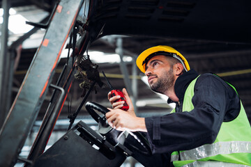 Industrial worker driving a forklift in the factory. Engineer is working and maintaining in the warehouse.