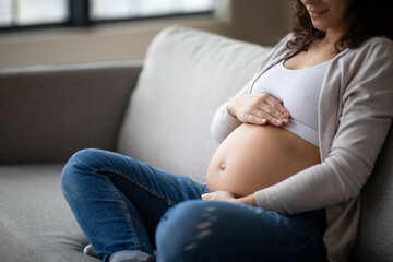 Prenatal Time. Unrecognizable Pregnant Woman Sitting On Couch And Embracing Her Belly