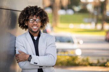 Portrait of successful black businessman posing with folded hands, standing near business center outdoors, free space