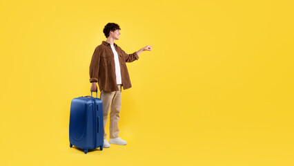 Man With Travel Suitcase Pointing Finger At Copyspace, Yellow Background