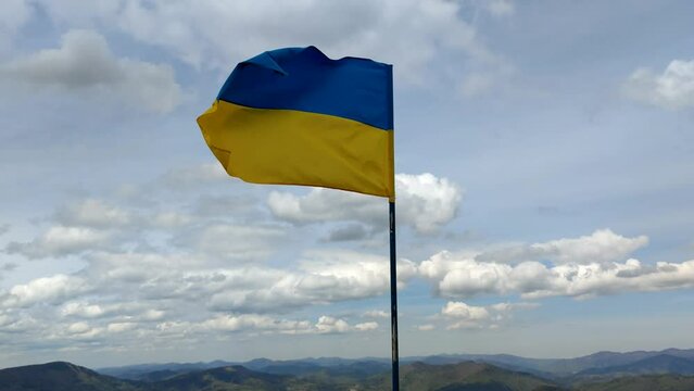 Ukraine flag waving on the top of Zahar Berkut in Carpathian Mountains, ukrainian state symbol, blue and yellow flag with cloudy sky on background. 
