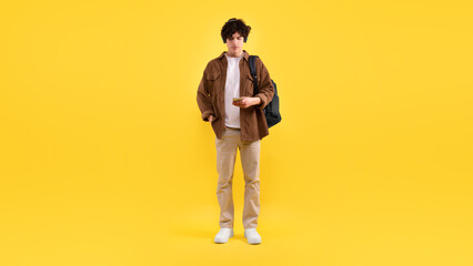 Student Guy Using Smartphone Listening Music Wearing Headphones, Yellow Background