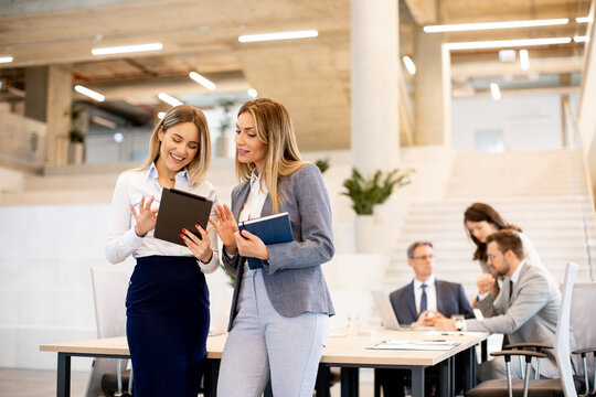 Two Young Business Women Looking At Financial Results On Digital Tablet In Front Of Their Team At The Office