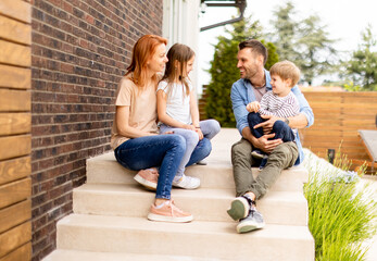 Family with a mother, father son and daughter sitting outside on the steps of a front porch of a brick house