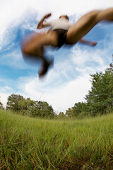 Fototapeta na wymiar Male runner jumping and running on meadow against blue sky and clouds; blur effect, fish-eye lens. Copy-space at the bottom.