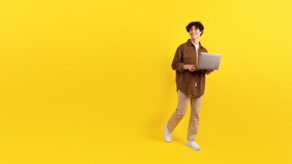 Fototapeta na wymiar Smiling Guy Holding Laptop Looking Aside Surfing Web, Yellow Background