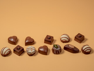 Assorted gourmet pralines in white, dark and milk chocolate. Chocolate candies on an orange background.