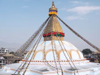 Buddhist stupa with prayers flags and a yellow lotus painted in the dome and  city in the background.