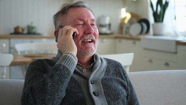 Happy middle aged senior man talking on smartphone with family friends. Older mature grandfather with cell phone talking with grown up children, resting at home. Older generation modern tech usage