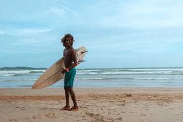 company of young guys Sri Lankans, Indians surfers on the ocean coast with a surfboard, sporty tanned body, smiling and running with a surfboard on the beach on a sunny summer day, ready to surf.