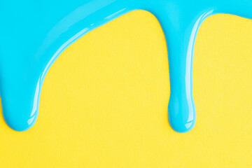 Light blue liquid drops of paint color flow down on yellow paper background. Blue paint dripping on the yellow wall with copy space.