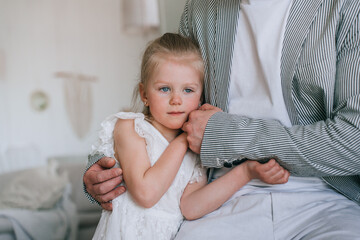 Cropped shoot of father calming little blonde daughter frustrated, needs more attention. Upset little girl in white dress holding fathers hand at home. Affection, fatherhood. Confused preschooler. - Powered by Adobe