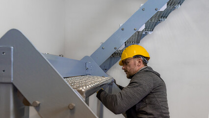 Installation of a steel staircase. The fitter fastens the grating stair step to the steel beam.