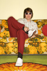 Caucasian mid-adult man sitting on colorful retro sofa wearing sunglasses looking bored.