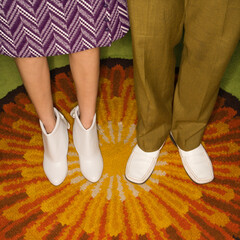 Close-up of Caucasian mid-adult male and female legs in vintage clothing against sunburst rug.