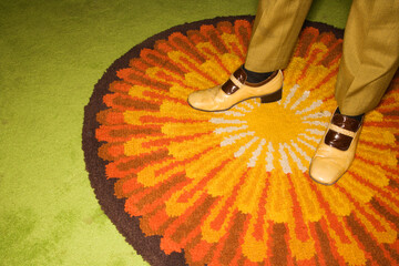 Close-up of Caucasian mid-adult male feet in vintage shoes against sunburst rug.