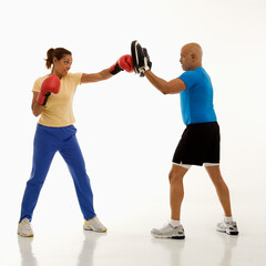 Mid adult multiethnic woman standing and punching focus mitts worn by multiethnic mid adult man.