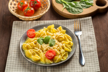 Pasta in a creamy sauce with cheese with a fork next to tomatoes, a knife and greens on a linen napkin.